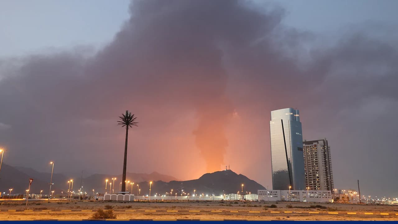 Large plume of smoke and fire rising near a city skyline in the Gulf region after a missile or drone strike, with buildings and streetlights visible in the foreground.