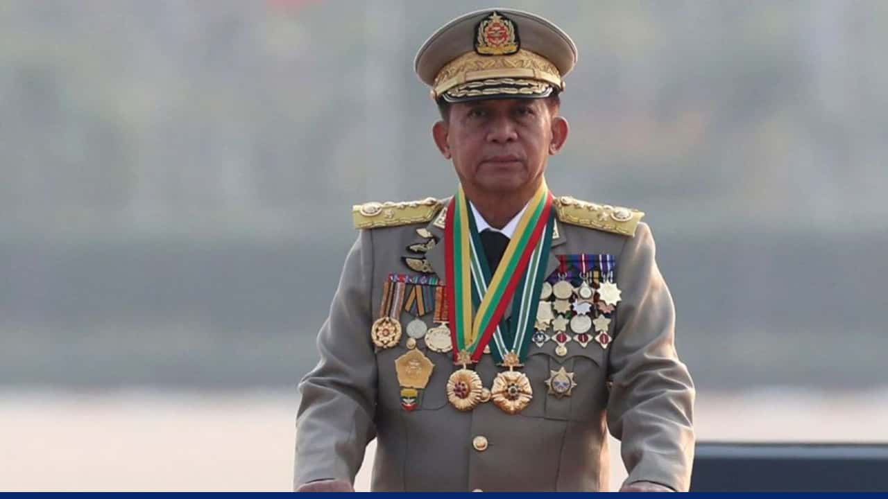 A decorated military officer in full uniform and cap, wearing numerous medals and ribbons, standing upright outdoors against a blurred background.