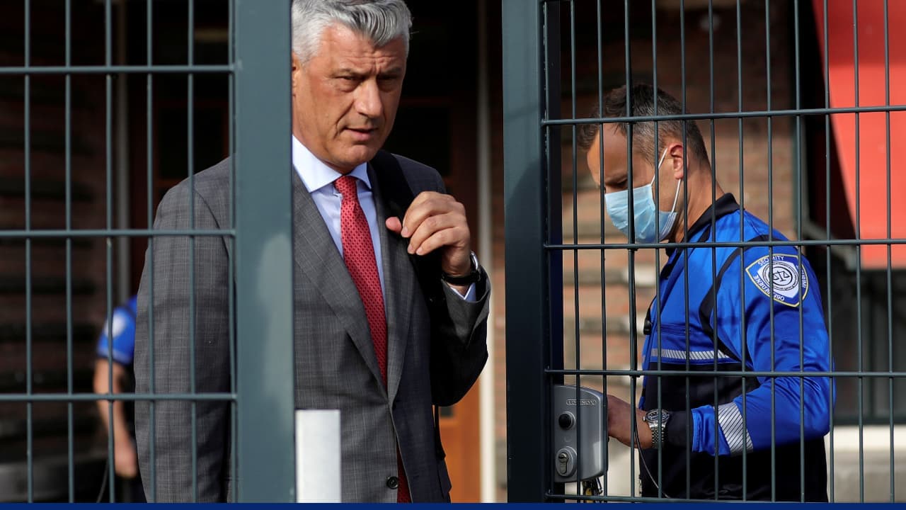 Suited gray-haired man exits metal gate with masked officer