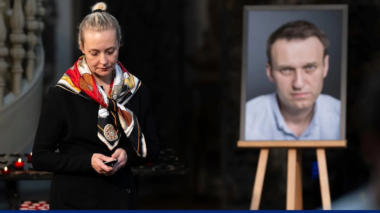 Woman stands beside portrait of Alexei Navalny