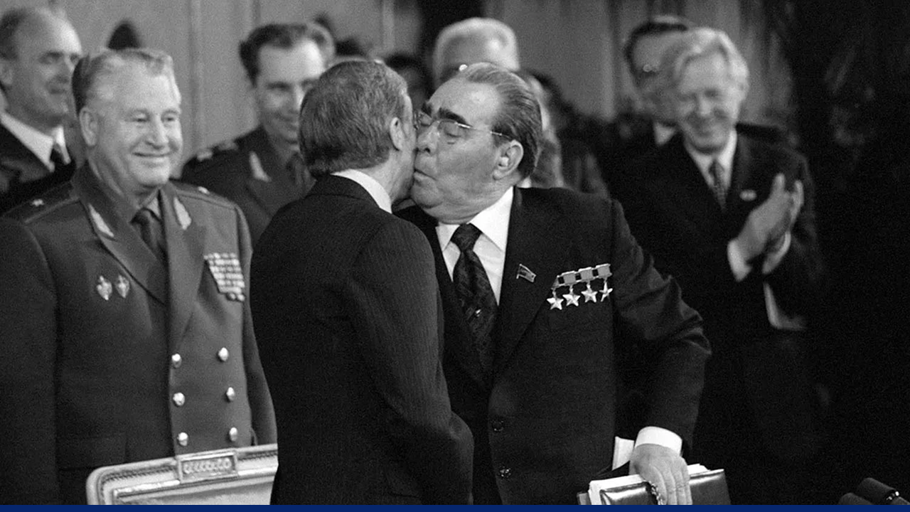 Soviet leader Leonid Brezhnev kisses Jimmy Carter on the cheek during a formal diplomatic event, surrounded by applauding officials.