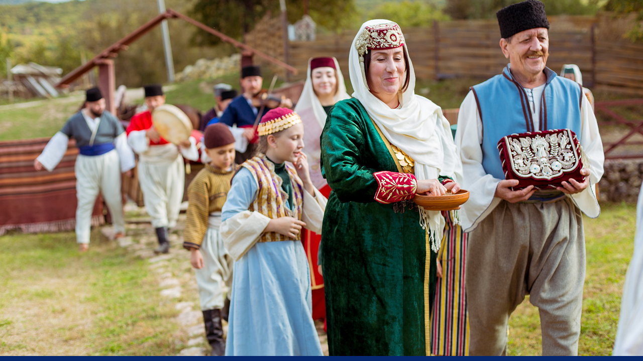 A group of Crimean Tatars dressed in traditional clothing participates in a festive wedding procession with music and ceremonial items.