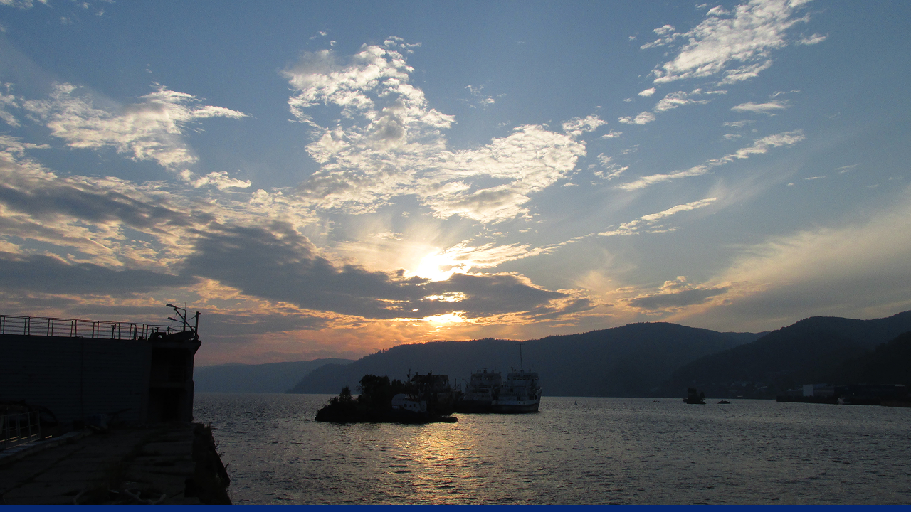 Sunset over Lake Baikal with silhouetted ships and hills.